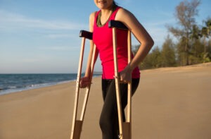 woman walking with crutches on beach